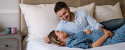 couple laying on bed holding smiling prenatal vitamins on night stand - Kosher prenatal vitamins for him and her - WeNatal prenatal vitamins